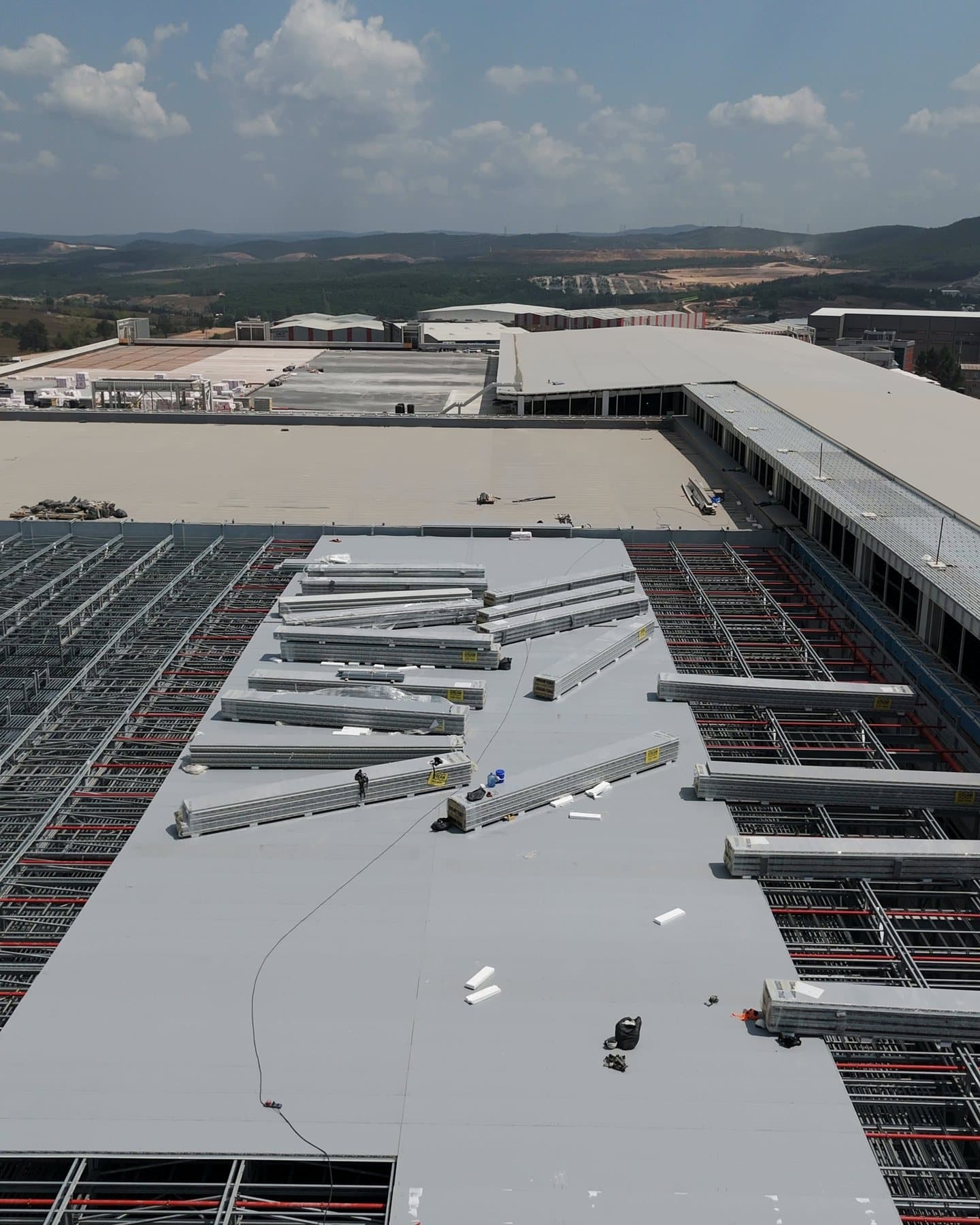 Panels being laid on the roof of a rack-clad warehouse, aerial view