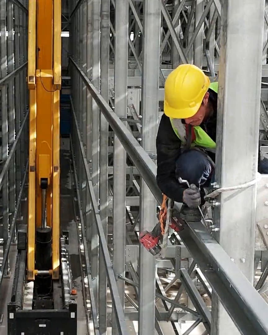 Fitter working high on the racking in an automated warehouse (ASRS) aisle