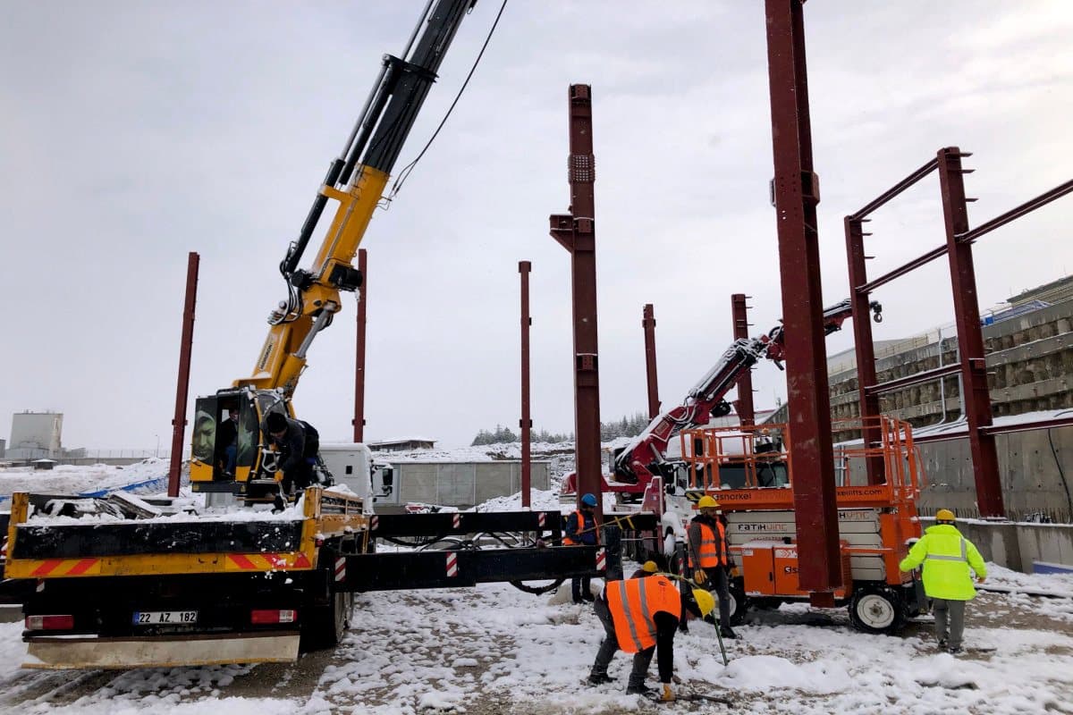 Crew erecting steel columns by crane on a snow-covered site